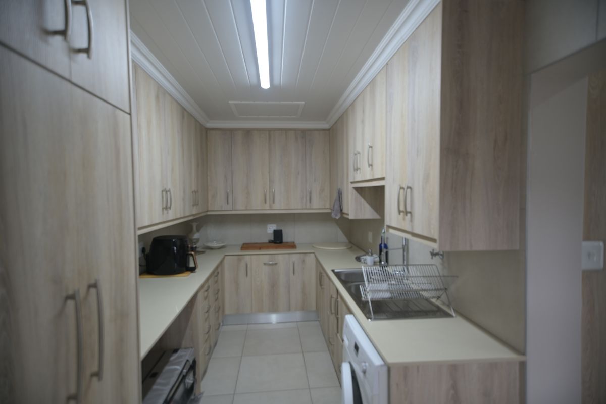 A functional galley-style kitchen featuring light wood-look cabinetry, stone countertops, and tiled flooring with ample storage space.