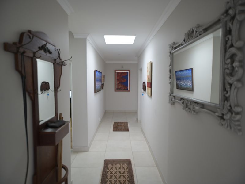 A bright, neutral-toned hallway featuring tiled flooring, coved cornicing, and a central skylight providing natural illumination.