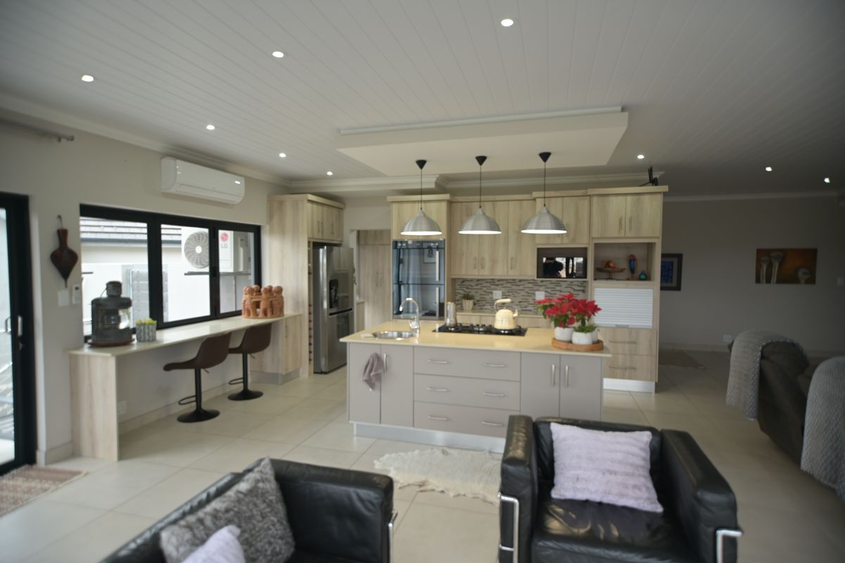 Modern open-plan kitchen featuring a central island, light wood cabinetry, integrated appliances, and a breakfast bar, seamlessly flowing into the living area.