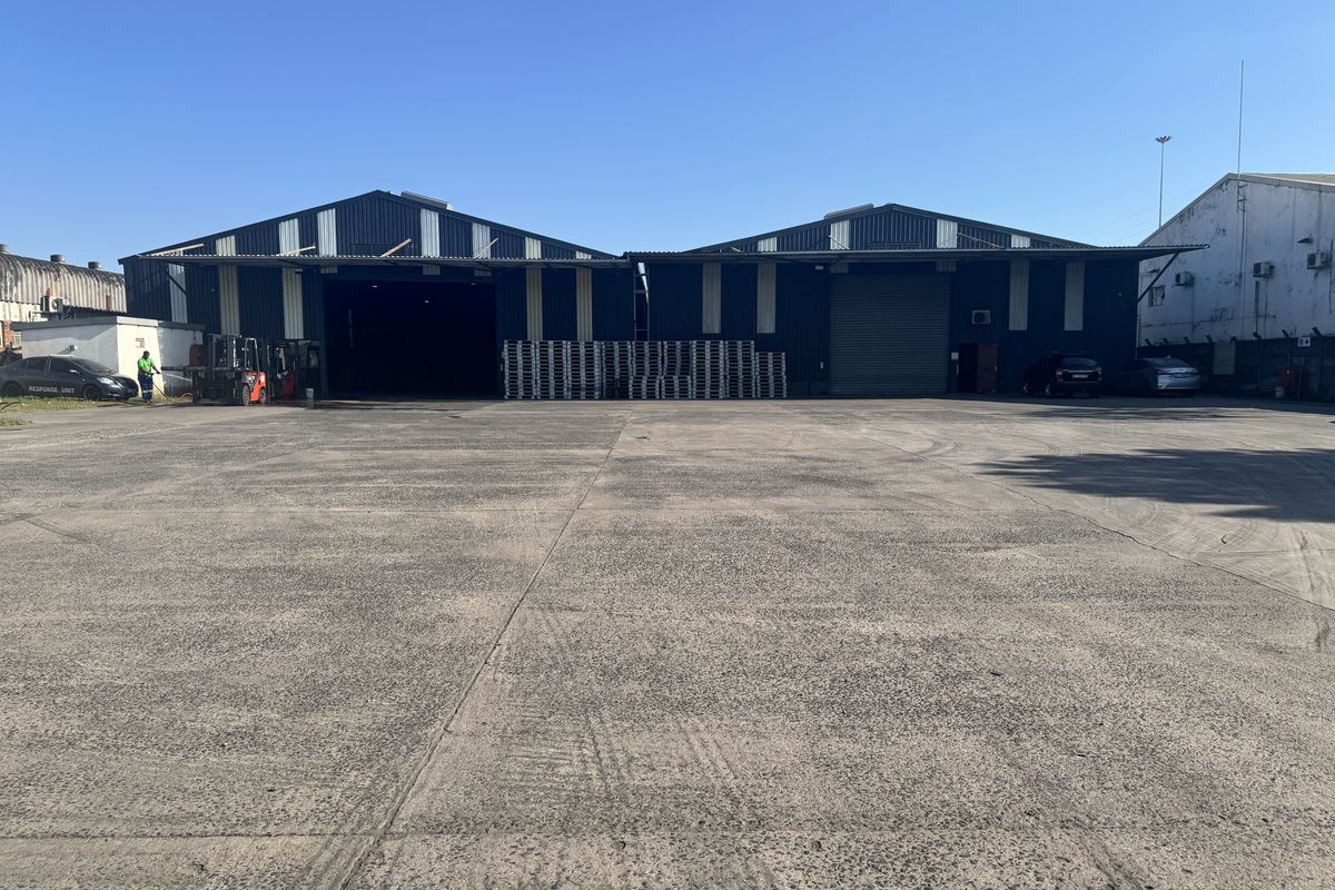Industrial warehouse facility featuring large concrete yard space, metal cladding, and multiple roller shutter access points for logistics and storage operations.