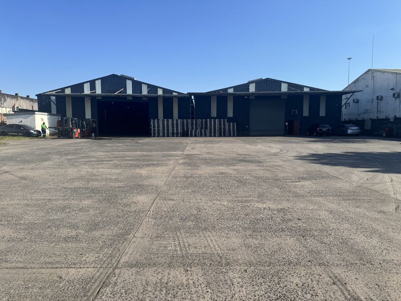 Industrial warehouse facility featuring large concrete yard space, metal cladding, and multiple roller shutter access points for logistics and storage operations.