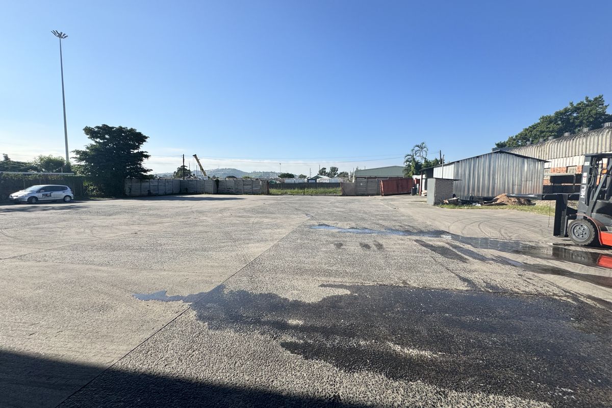 Expansive industrial concrete yard featuring perimeter fencing, high mast lighting, and adjacent metal storage structure.
