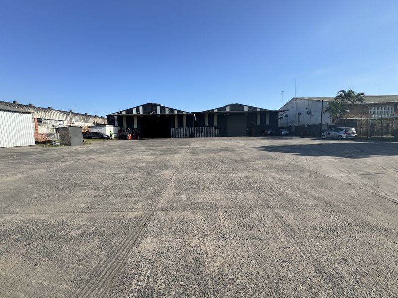 Spacious industrial yard with large concrete hardstand area providing access to multiple warehouse units with metal cladding and roller shutter doors.