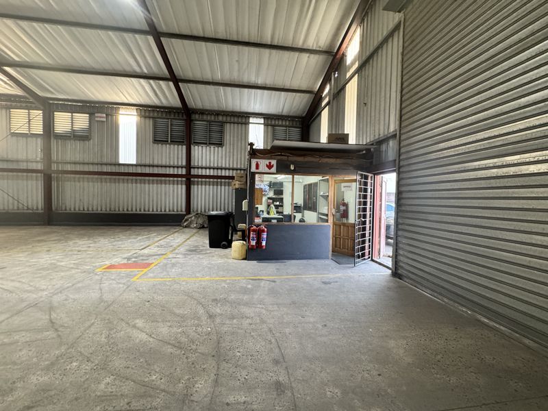 Spacious industrial warehouse unit featuring high ceilings, corrugated metal walls, concrete flooring, and a dedicated built-in office enclosure with security access.