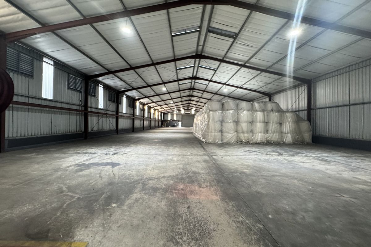 Spacious industrial warehouse featuring a steel portal frame, concrete flooring, and natural light through roof skylights, suitable for storage or manufacturing operations.