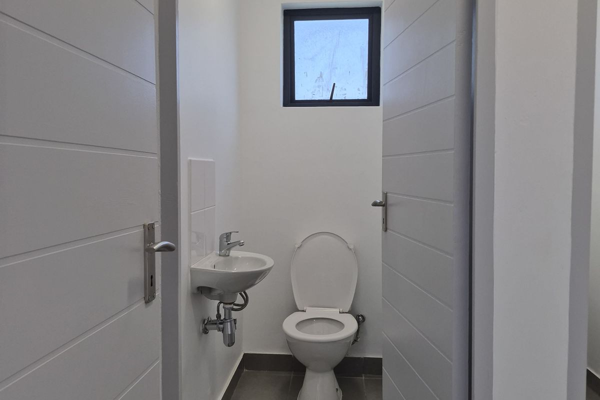 A clean, modern guest bathroom featuring a wall-mounted basin, a standard toilet, and tiled flooring, accessed through a doorway.