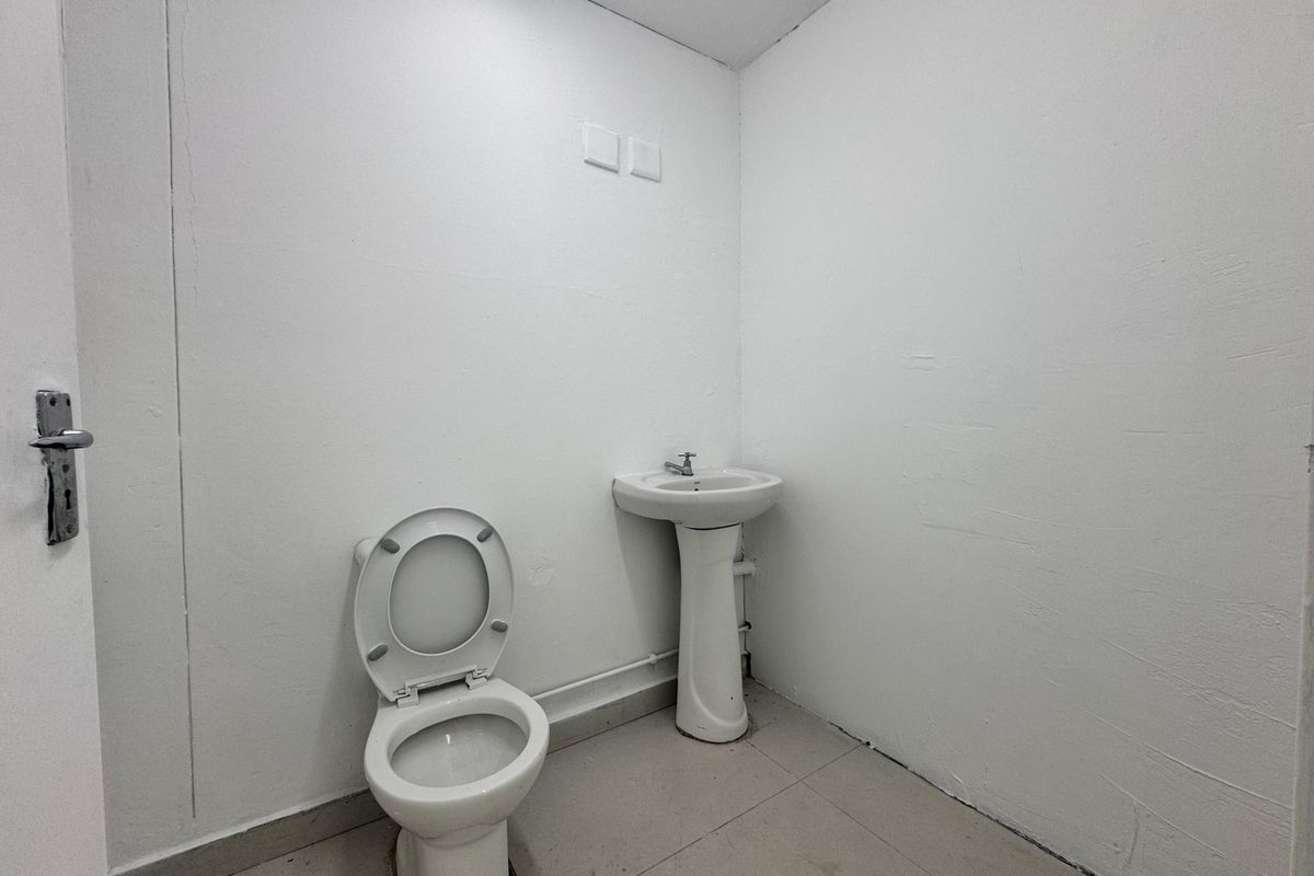A functional office restroom featuring a pedestal sink and standard toilet with tiled flooring and plain white walls.
