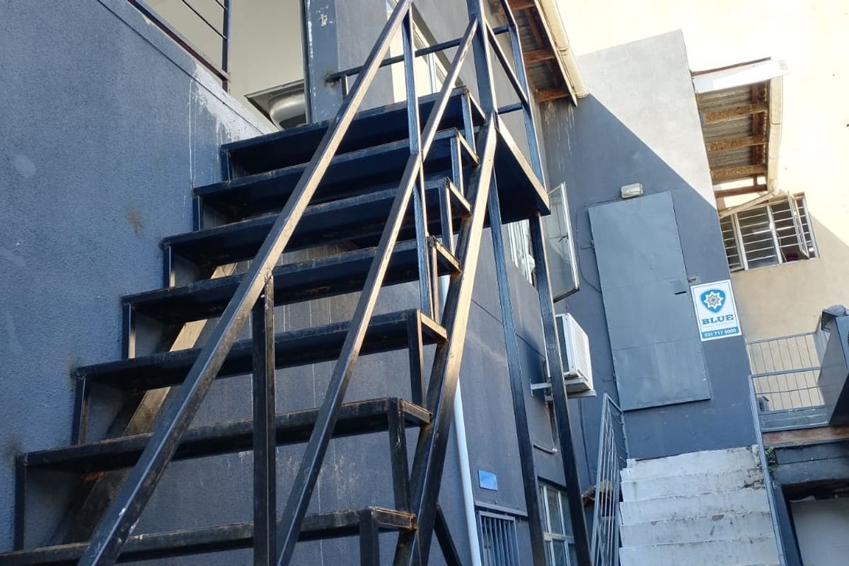 Exterior view of a commercial building featuring a metal staircase, external wall finishes, and security signage.