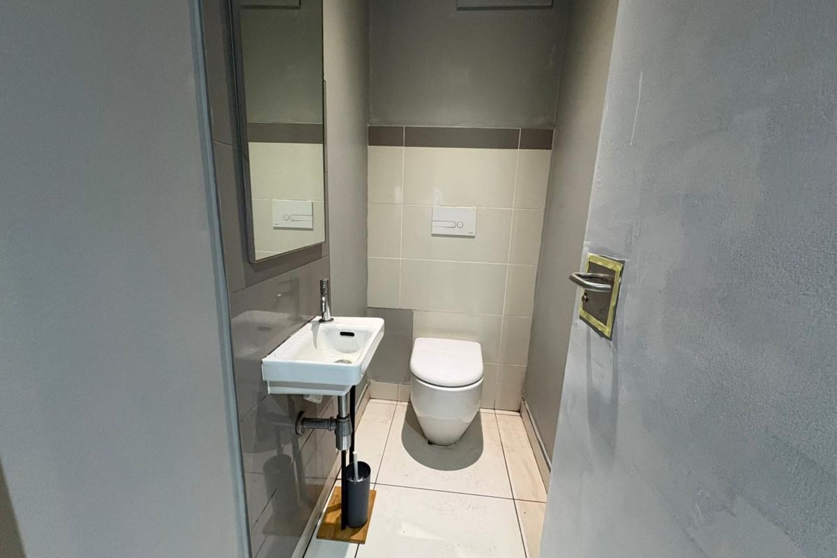 A compact guest bathroom featuring a wall-mounted toilet, a small wall-hung basin, and neutral tiled flooring.