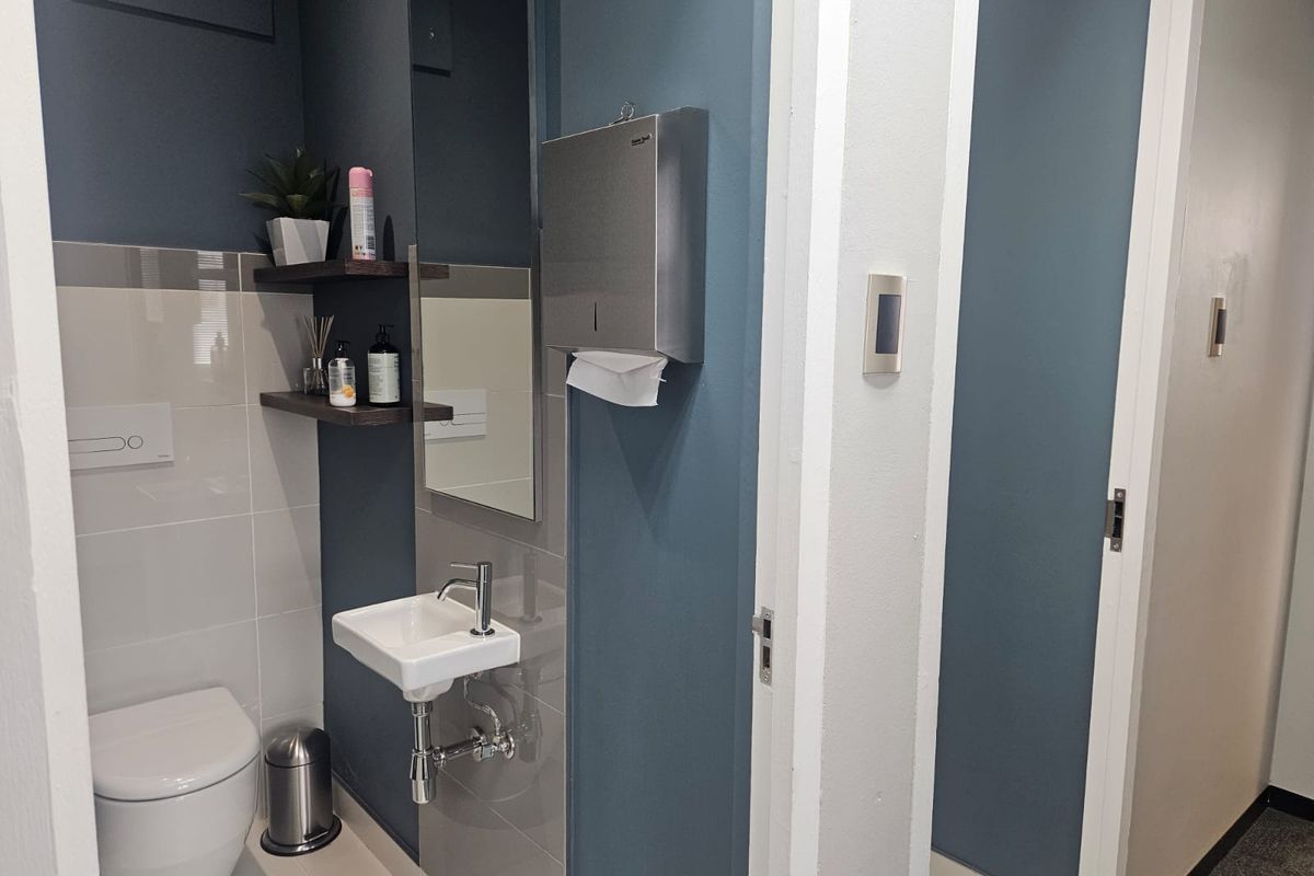 Modern office restroom featuring a wall-mounted basin, sleek blue accent walls, tiled splashback, and a stainless steel paper towel dispenser.