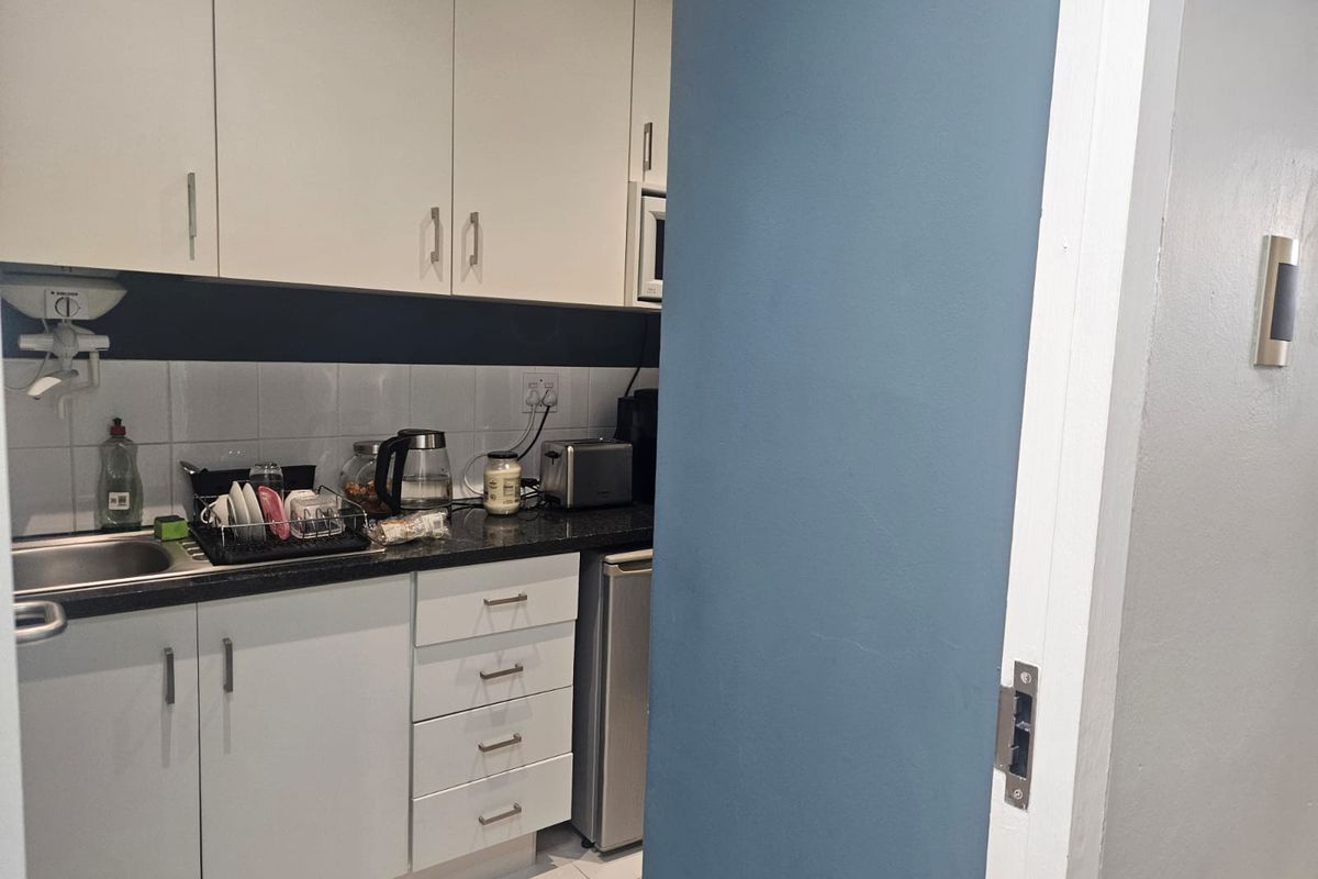 A compact office kitchenette featuring white cabinetry, dark countertops, a stainless steel sink, and tiled backsplash.