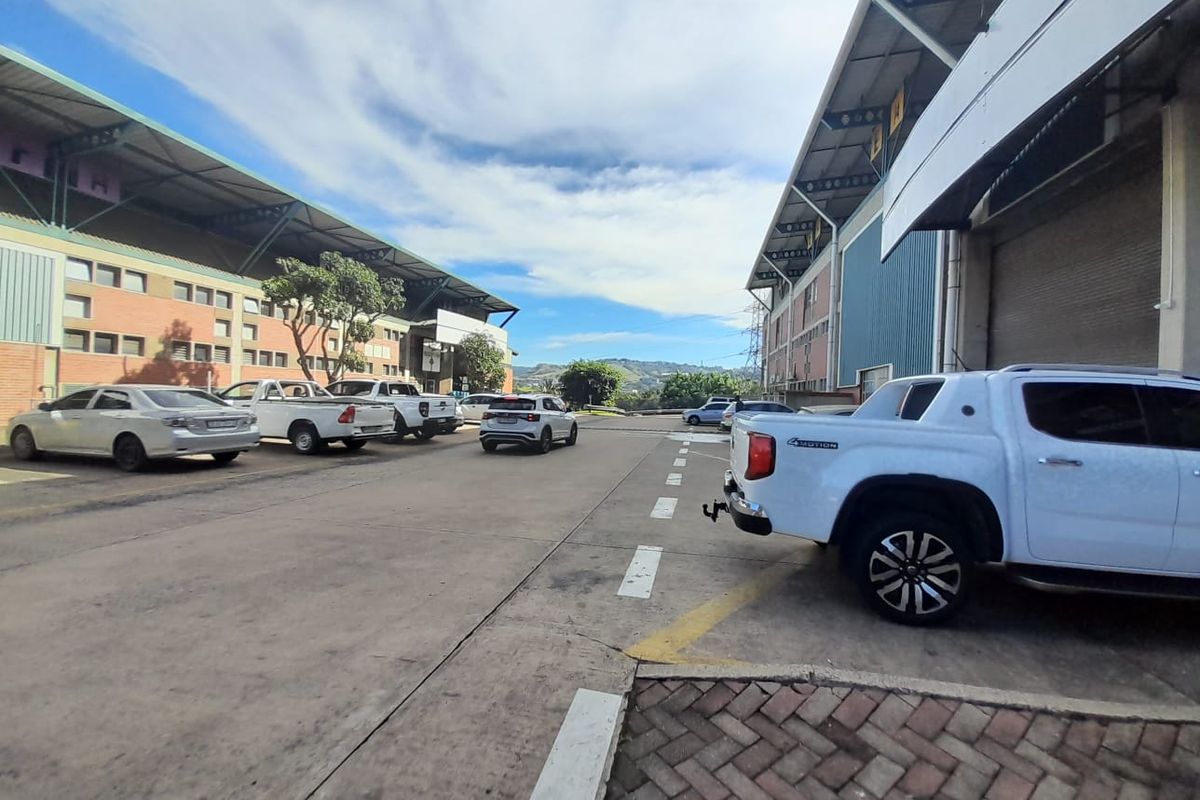 Exterior view of an industrial warehouse complex featuring concrete driveways, paved parking bays, and large roller shutter access doors.