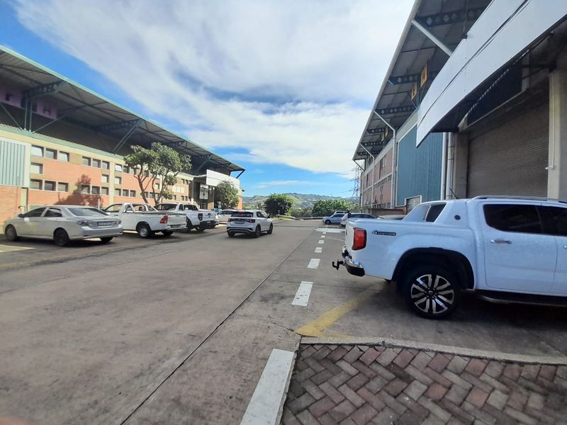 Exterior view of an industrial warehouse complex featuring concrete driveways, paved parking bays, and large roller shutter access doors.