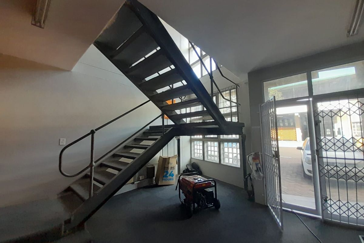 Industrial entrance area featuring a prominent metal staircase, secure glass door with security gate, and ample natural light through multi-pane windows.