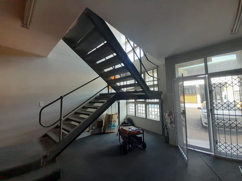 Industrial entrance area featuring a prominent metal staircase, secure glass door with security gate, and ample natural light through multi-pane windows.