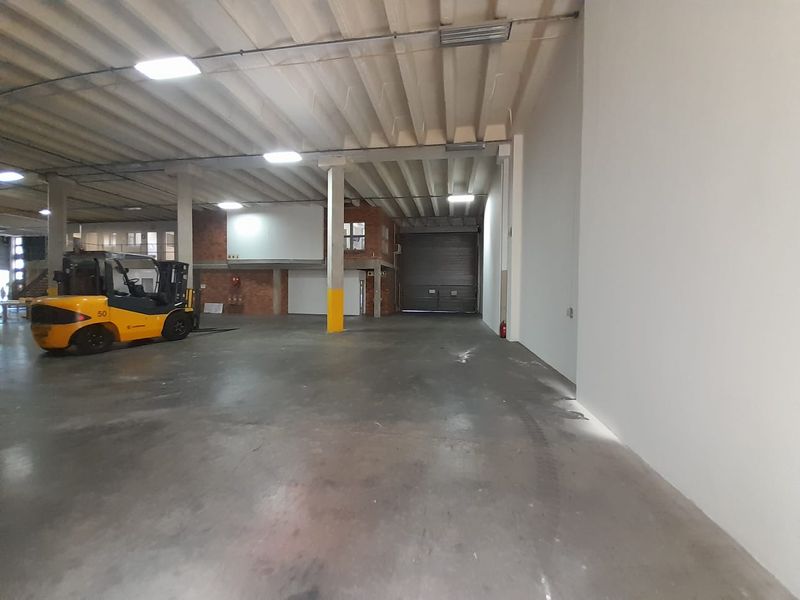 Spacious industrial warehouse unit featuring high ceilings, concrete flooring, a mezzanine level, and a large roller shutter door for easy access.