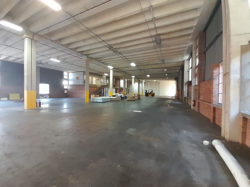 Spacious industrial warehouse area featuring high ceilings, exposed brickwork, concrete flooring, and structural support columns, suitable for various commercial or storage applications.