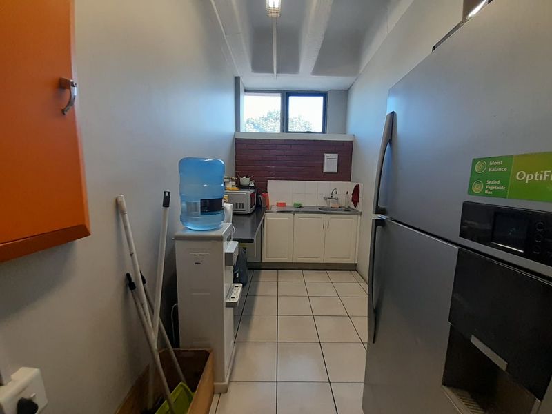 A functional scullery area featuring built-in cabinetry, a stainless steel sink, and tiled flooring with an exposed brick splashback.