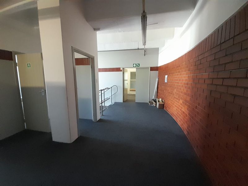 A spacious industrial hallway featuring exposed brick walls, carpeted flooring, and functional overhead lighting, providing access to multiple internal rooms.