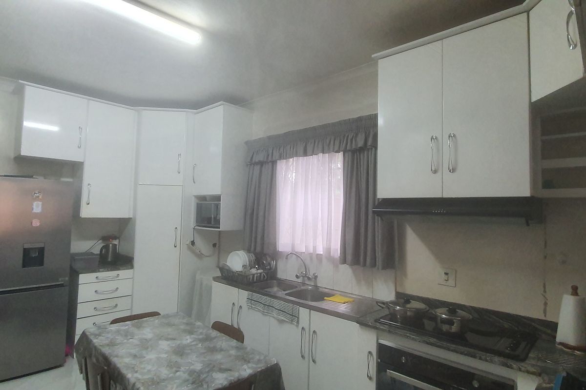Functional kitchen featuring white built-in cabinetry, integrated oven, hob, extractor fan, and stainless steel sink with tiled flooring.
