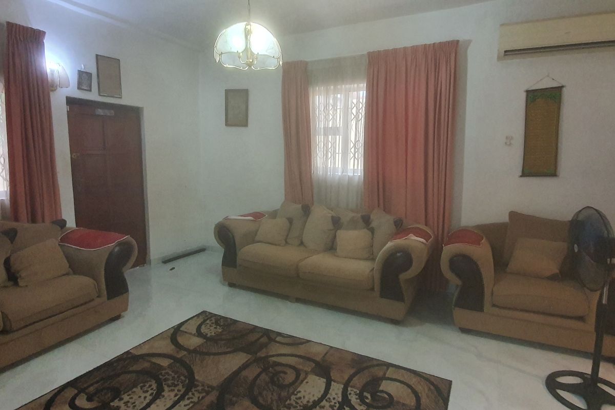 A living room featuring tiled flooring, a wall-mounted air conditioning unit, and security-gated windows, providing a functional and secure space.