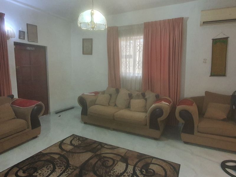 A living room featuring tiled flooring, a wall-mounted air conditioning unit, and security-gated windows, providing a functional and secure space.