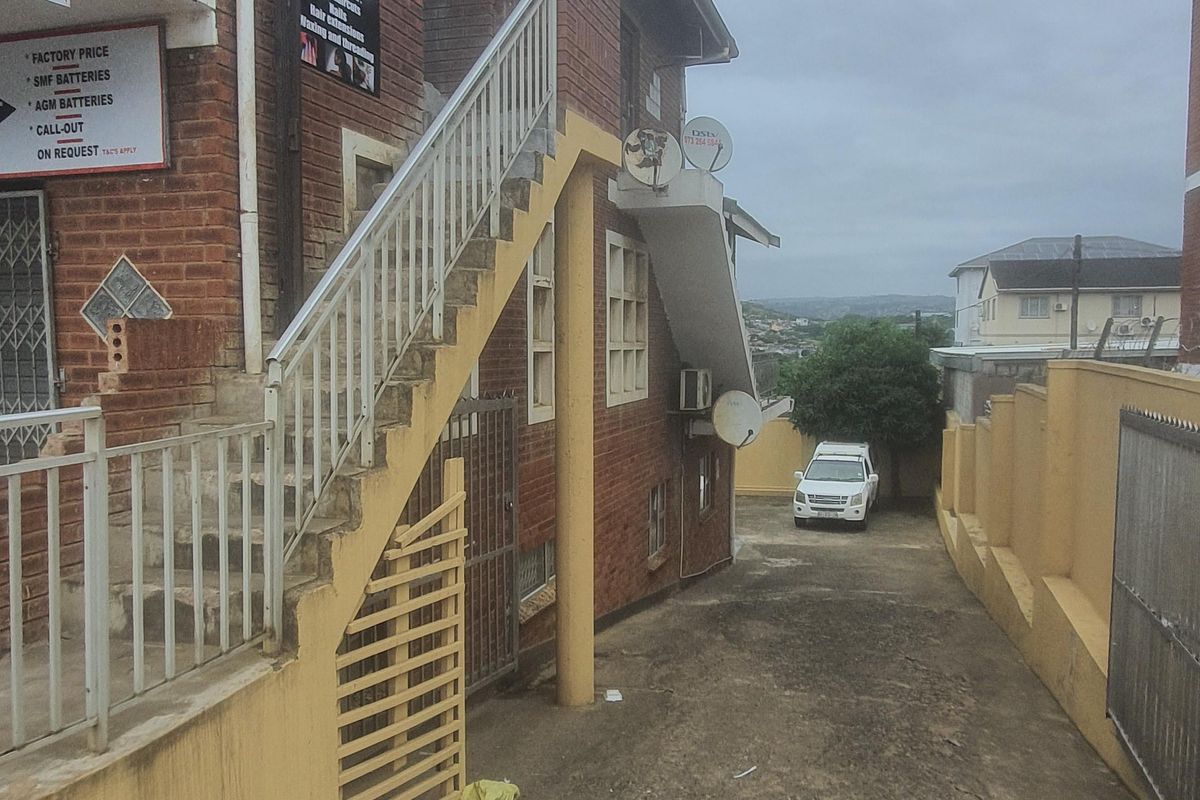 Side view of a commercial brick building featuring an external staircase, concrete driveway, and boundary wall access.