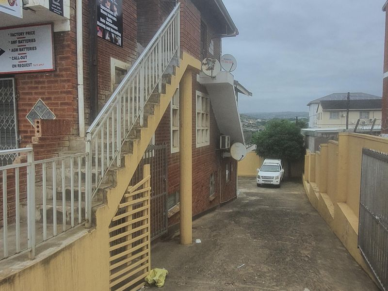 Side view of a commercial brick building featuring an external staircase, concrete driveway, and boundary wall access.