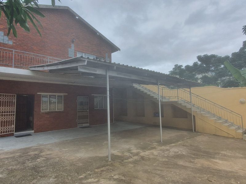 Rear exterior view of a commercial property featuring a brick facade, covered carport area, and an external staircase leading to an upper level.