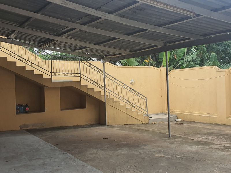 A spacious outdoor covered area featuring a concrete staircase with wrought iron railings and a perimeter wall, suitable for parking or outdoor utility use.