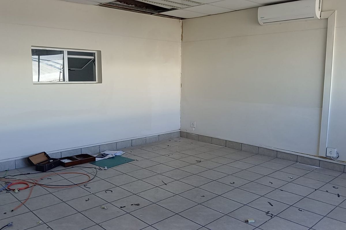 An empty office space featuring tiled flooring, a wall-mounted air conditioning unit, and a suspended ceiling requiring minor repairs.