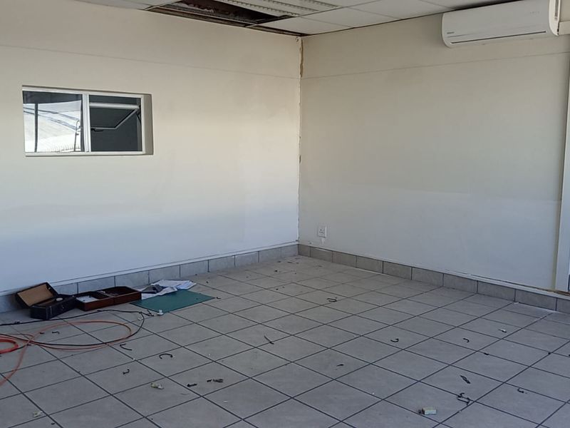 An empty office space featuring tiled flooring, a wall-mounted air conditioning unit, and a suspended ceiling requiring minor repairs.