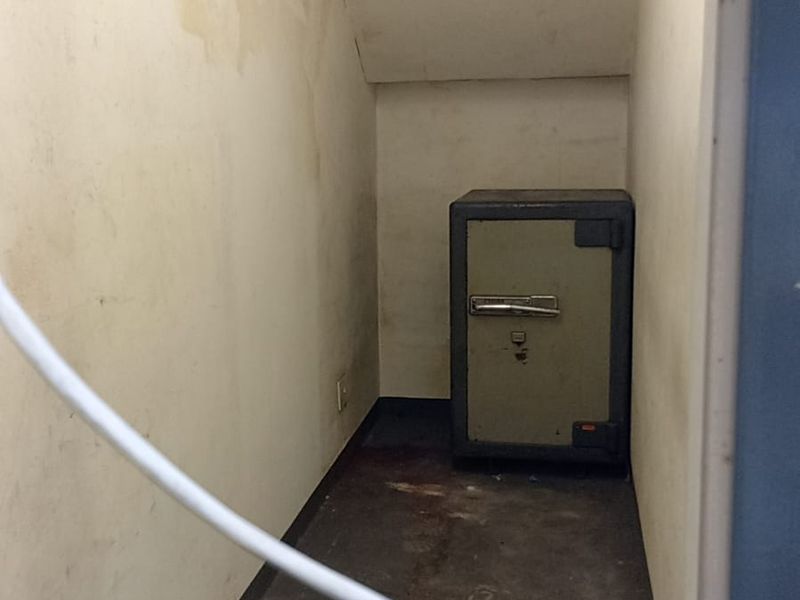 A small, utilitarian storage space featuring a built-in safe, ventilation grilles, and worn wall and floor finishes.