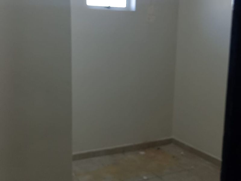 A small, empty utility space featuring tiled flooring and a single window, currently showing signs of wear and wall staining.