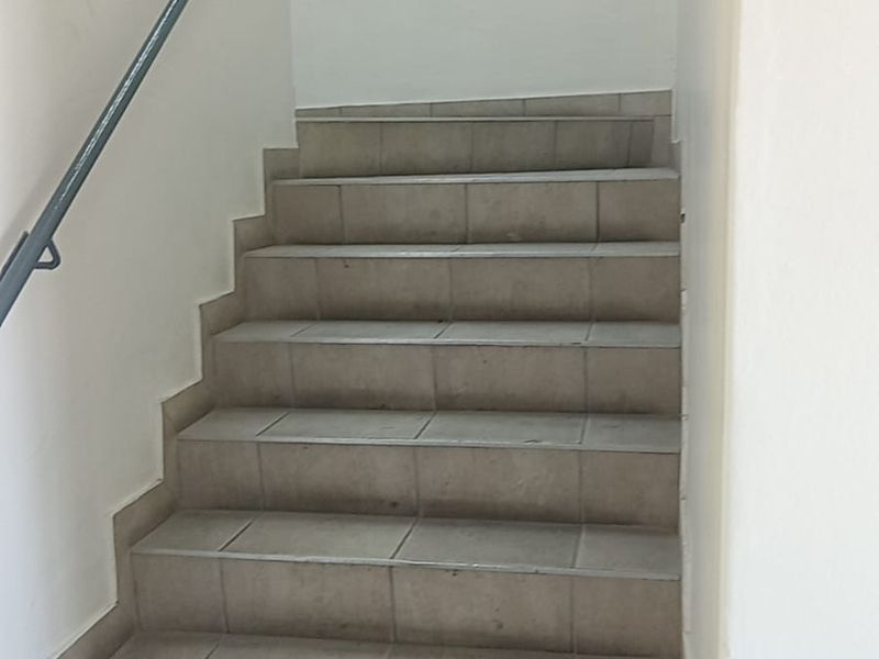 A functional interior staircase featuring tiled steps and a simple metal handrail, providing access between levels within the industrial property.