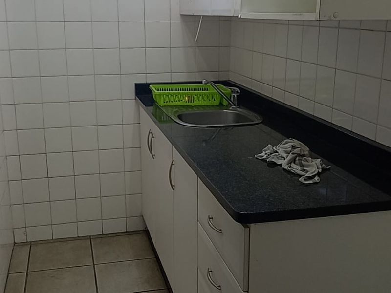 A functional scullery area featuring built-in cabinetry, a stainless steel sink, dark laminate countertops, and tiled wall finishes.