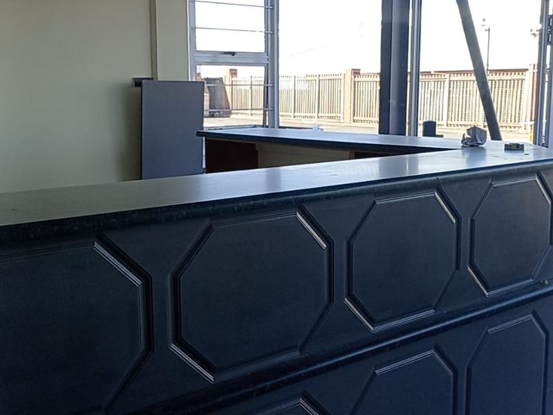 A professional reception area featuring a built-in counter, tiled flooring, and large windows providing natural light, suitable for an industrial or commercial office space.