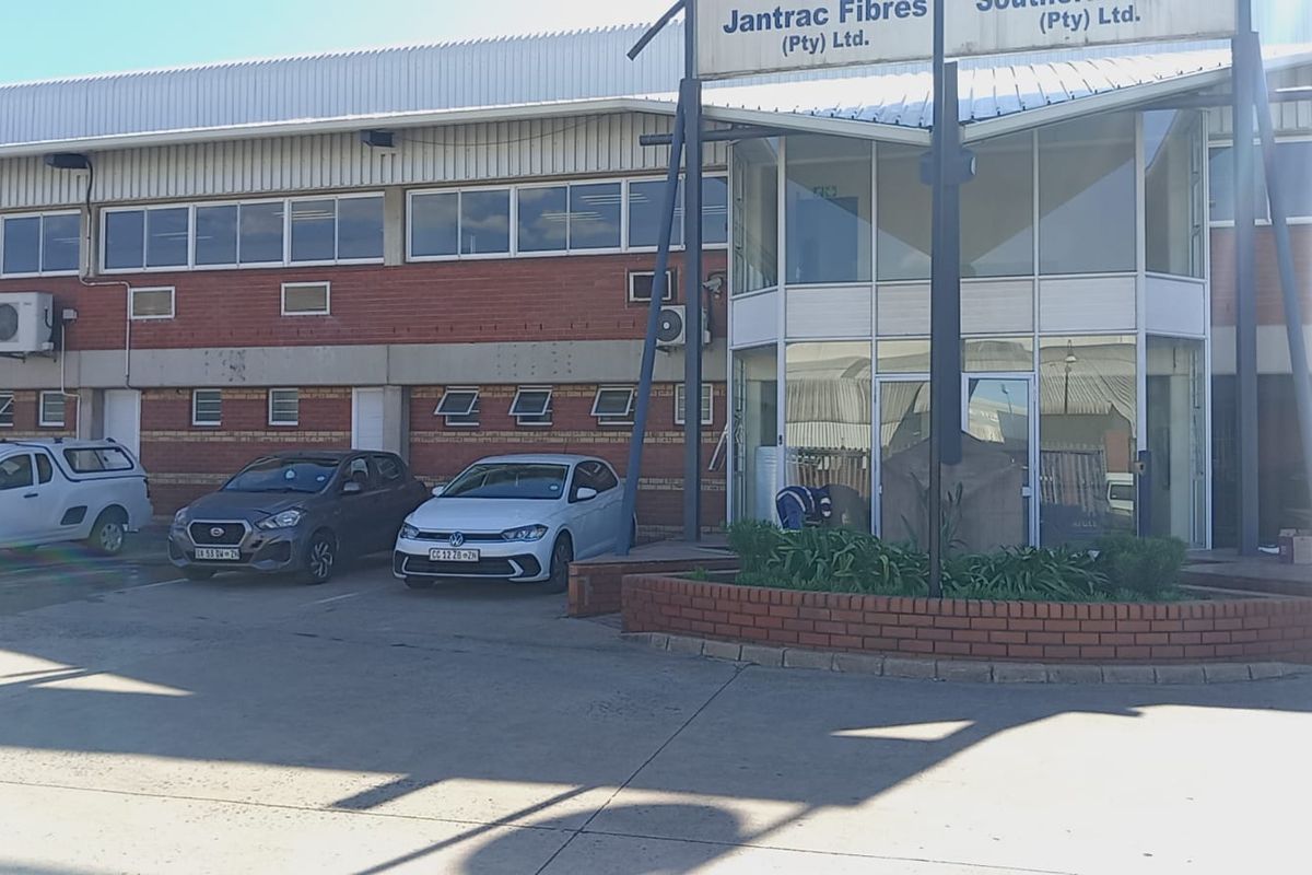 Front exterior view of an industrial property featuring a brick facade, metal roofing, and a prominent glass entrance foyer with paved parking.