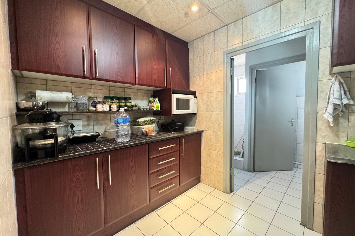 Functional kitchen area featuring dark wood-grain cabinetry, tiled splashbacks, and tiled flooring, with direct access to an adjacent utility or laundry space.
