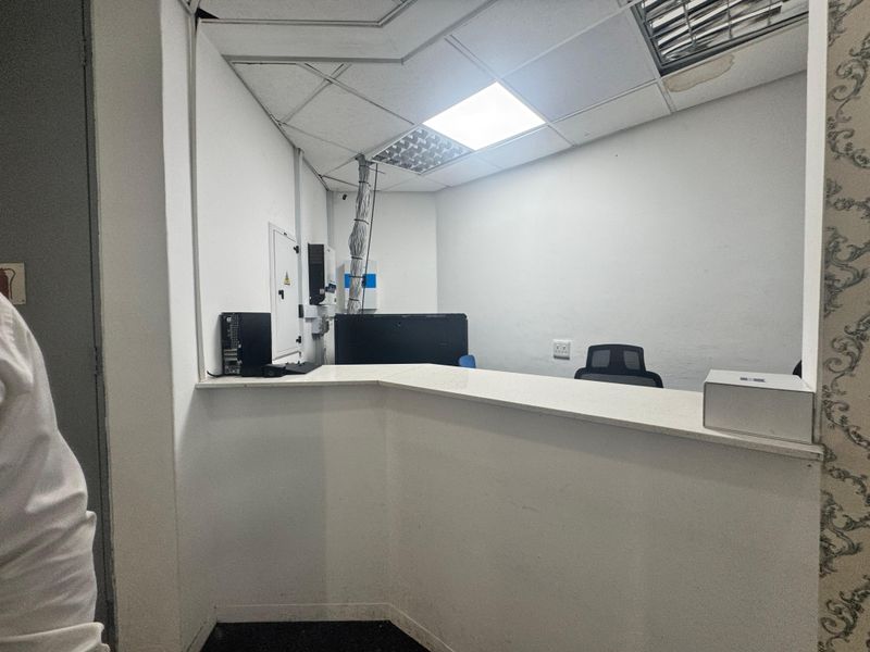 A functional office reception area featuring a built-in service counter, drop ceiling with integrated lighting, and exposed electrical infrastructure.