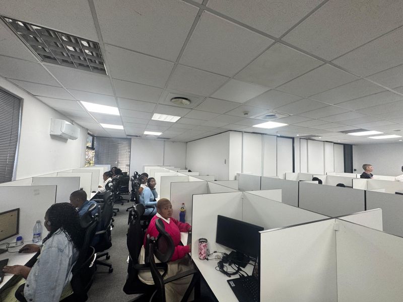 Open-plan office space featuring modular workstations, suspended acoustic ceiling tiles, and wall-mounted air conditioning unit.