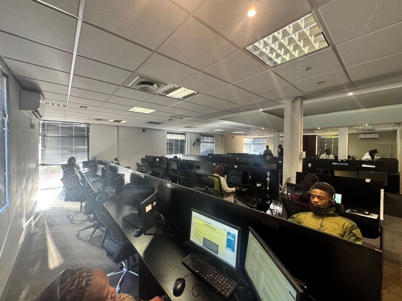 Spacious open-plan office environment featuring suspended acoustic ceiling tiles, recessed lighting, and integrated workstation partitions suitable for a call center or collaborative workspace.