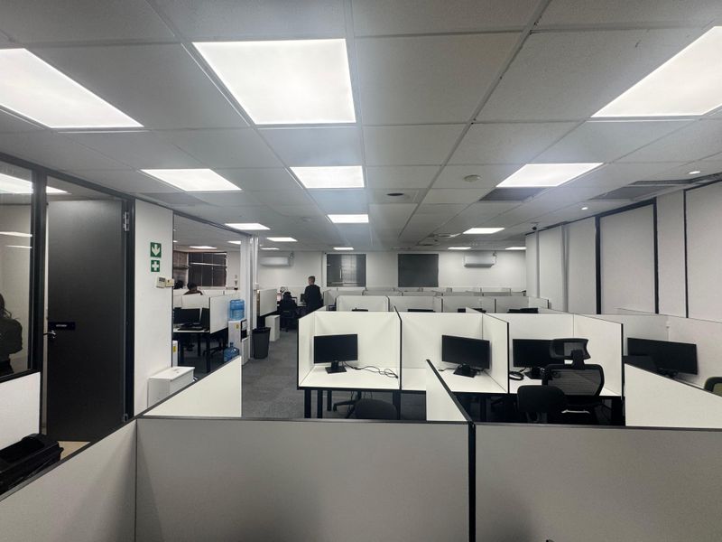 Open-plan office space featuring modular workstation cubicles, suspended acoustic ceiling tiles with integrated lighting, and carpeted flooring.