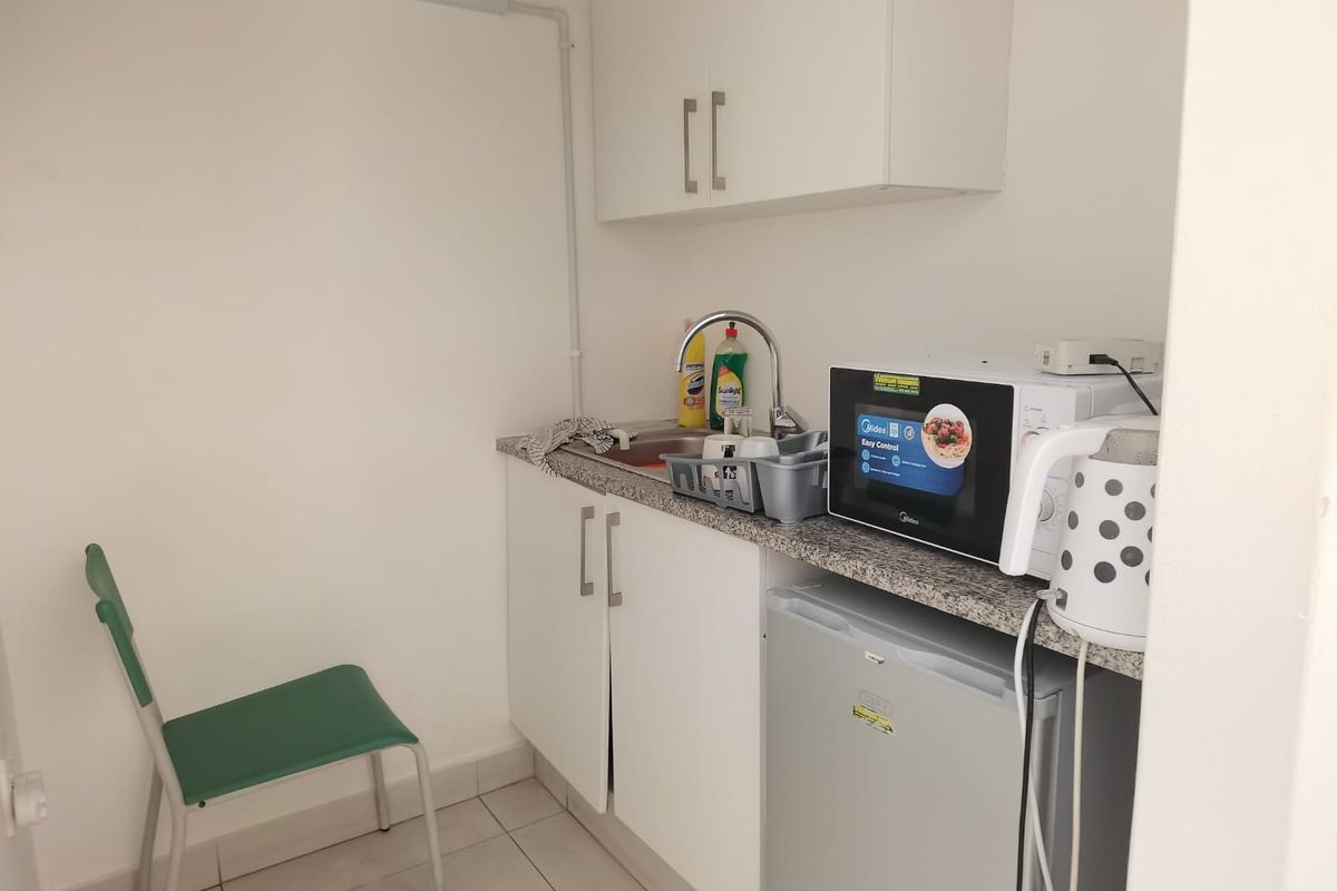 A compact kitchenette featuring white cabinetry, a granite-look countertop, a stainless steel sink, and tiled flooring.