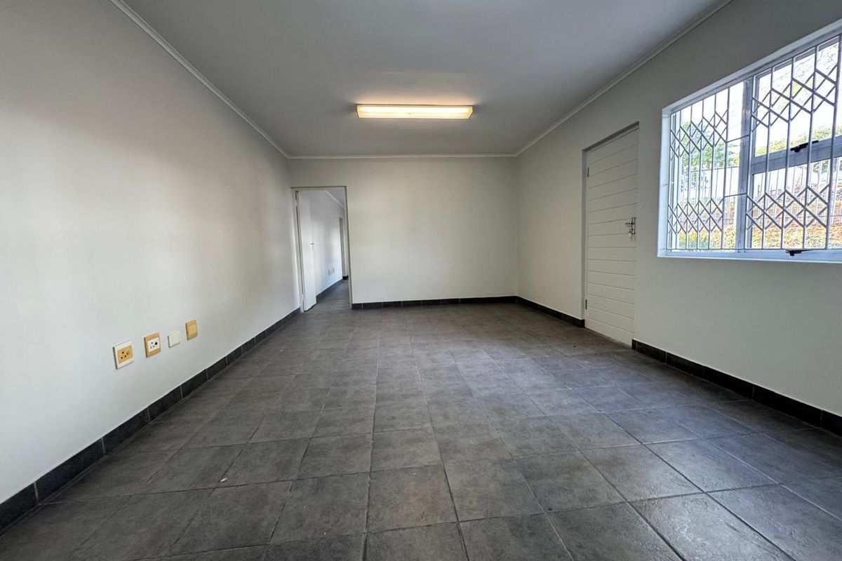 A clean, empty interior space featuring neutral tiled flooring, white walls, and a window fitted with security bars.