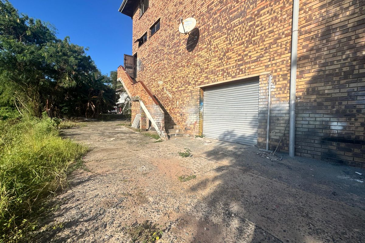 Exterior view of an industrial building featuring a brick facade, a roller shutter garage door, and an external staircase leading to an upper level.