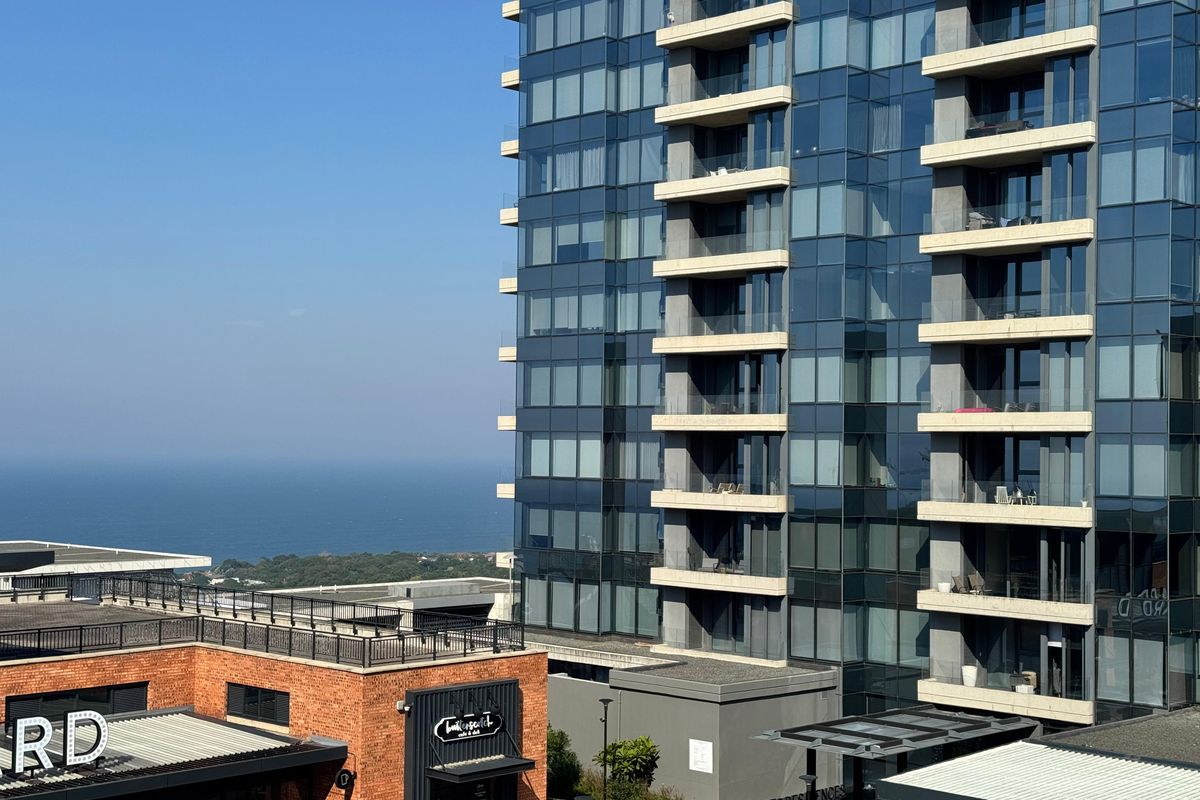 A high-rise glass facade office and residential building overlooking the ocean, featuring modern architectural design and integrated balcony structures.