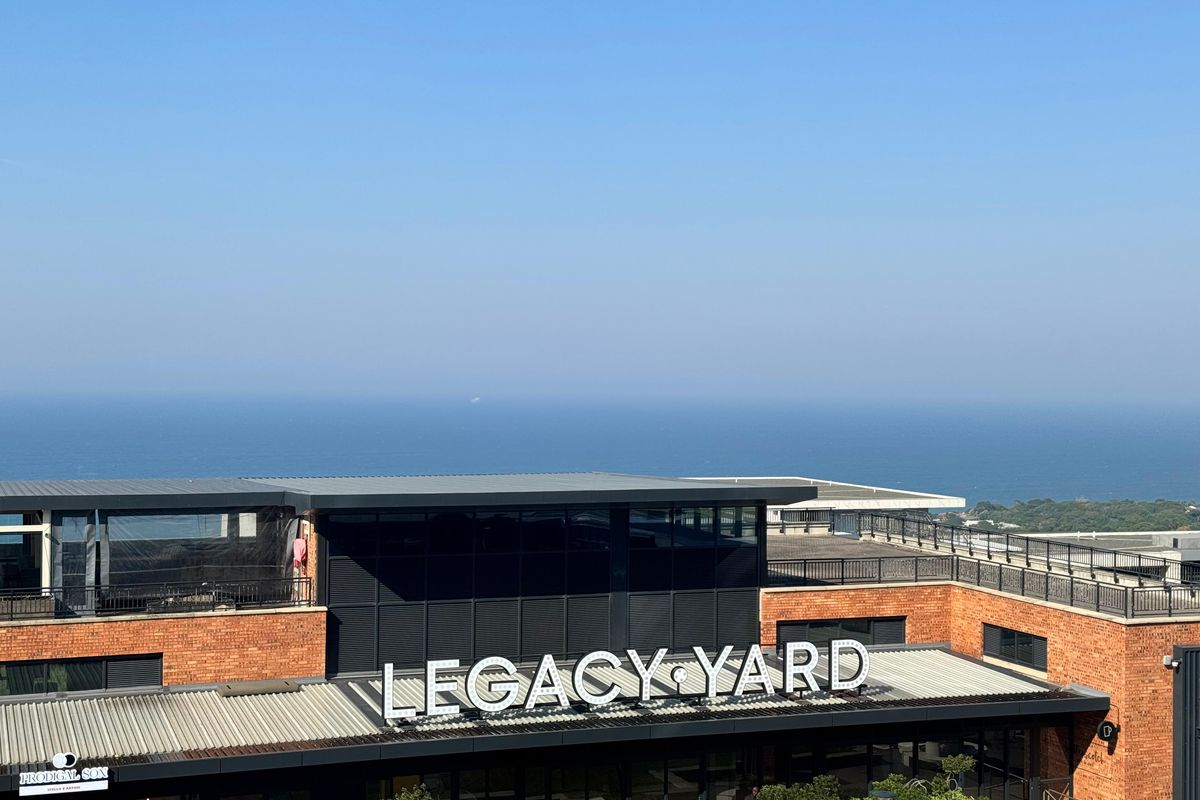 An elevated view of the Legacy Yard office complex, featuring modern brick architecture and a prominent rooftop signage overlooking the ocean.