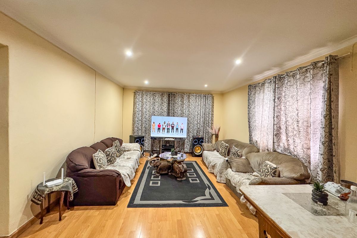 A spacious living room featuring laminate wood flooring, recessed ceiling lighting, and large windows dressed with patterned curtains.