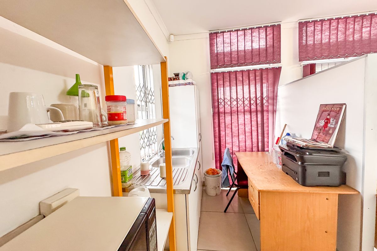 A functional kitchenette area featuring a stainless steel sink, built-in cabinetry, and vertical window blinds, suitable for a compact commercial office space.